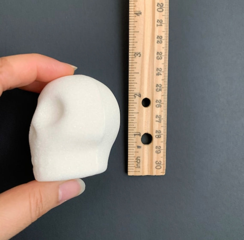 White blank sugar skull made of sugar held by a hand next to a wooden ruler on a dark background