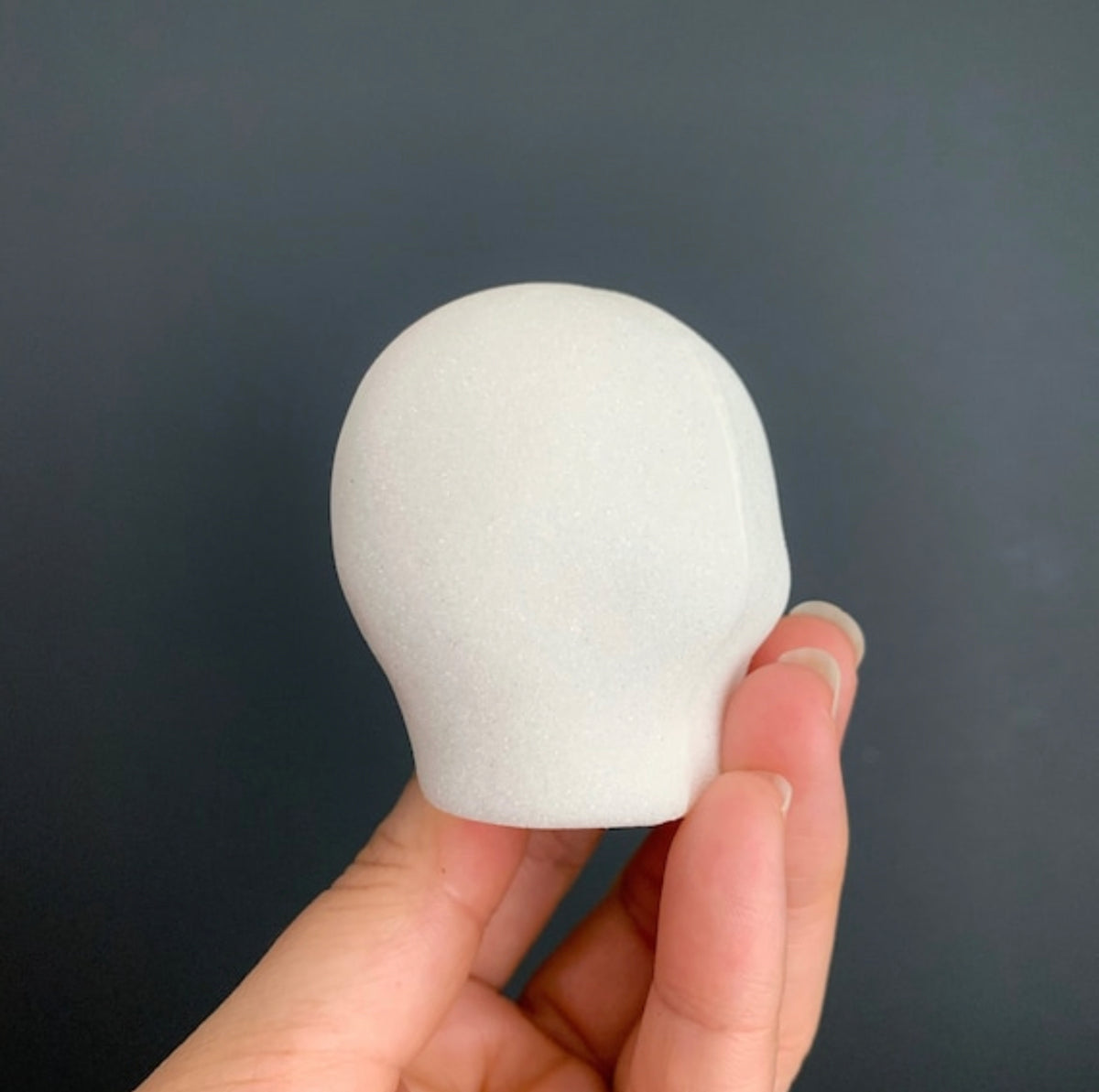 White blank molded sugar skull head held by a hand against a dark background