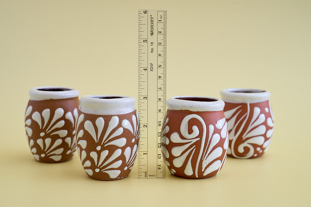 Four small brown and white patterned ceramic pots arranged on a beige background, with a measuring tape standing vertically between them for scale.