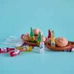 A miniature diorama setup featuring tiny toy beverage bottles and donuts on a terracotta tray, set against a solid turquoise background.